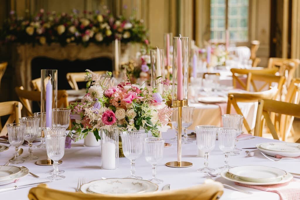 Décoration de table avec des bougeoirs dorés et un bouquet de centre de table contenant des fleurs couleur rose et lavande dans une coupe doré.