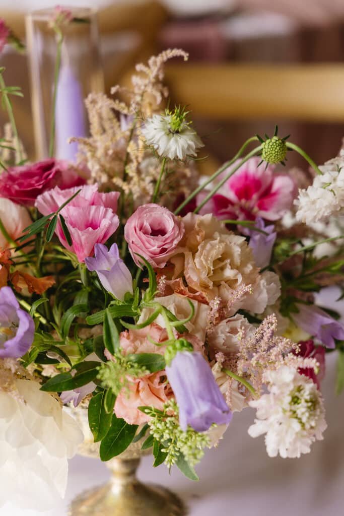 Bouquet de centre de table avec des fleurs rose et lavande. Le bouquet est dans une coupe sur pied dorée.