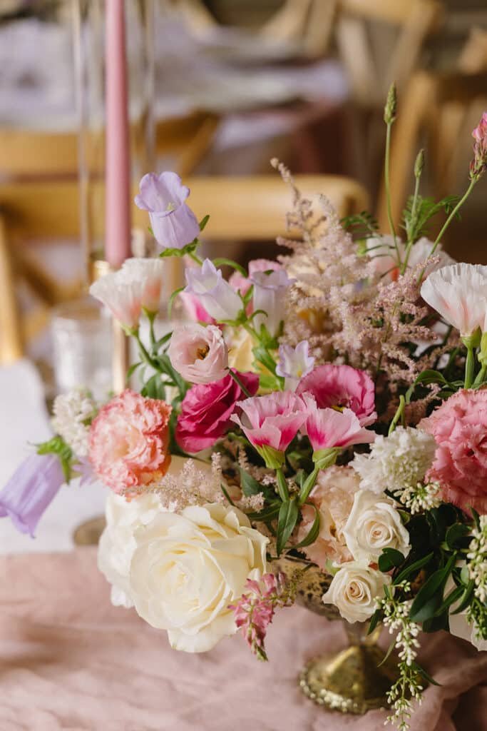 Bouquet de centre de table avec des fleurs rose et lavande. Le bouquet est dans une coupe sur pied dorée.